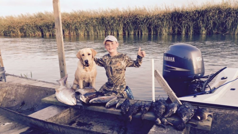 A boy and his dog out recreating on a boat in a marsh in Louisiana.